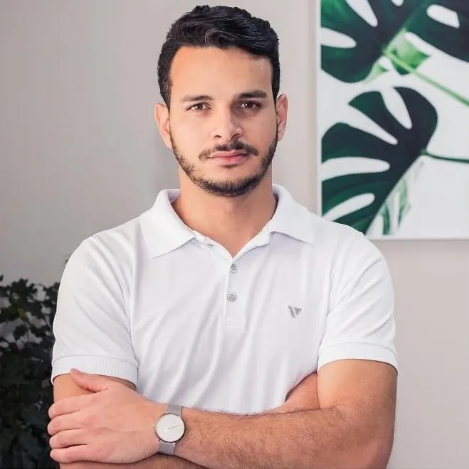 Ronney Ferreira de camisa polo branca, de braços cruzados, no estúdio